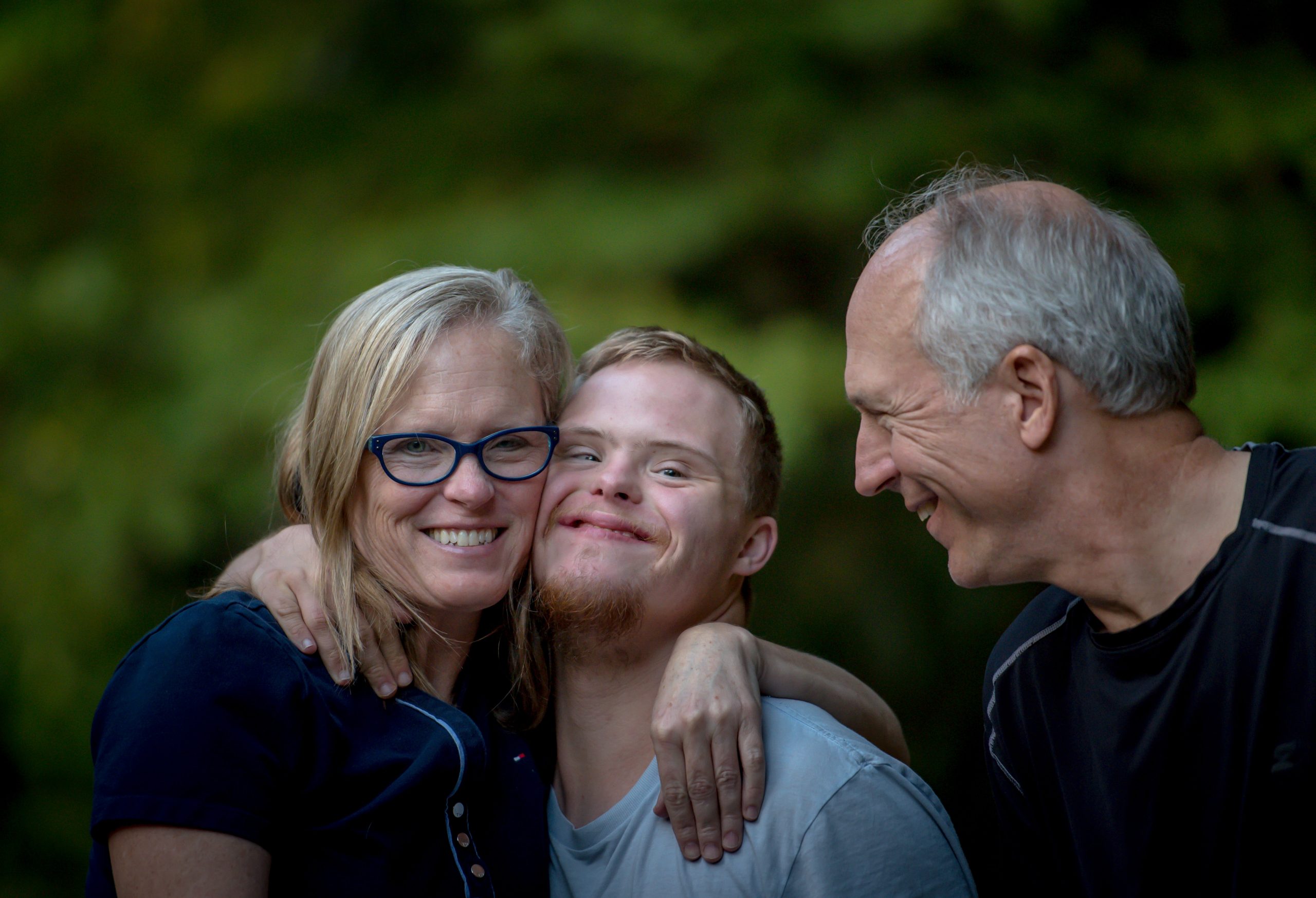 Image shows a family comprised of a woman (mom), a young adult with Down Syndrome and a man (dad).