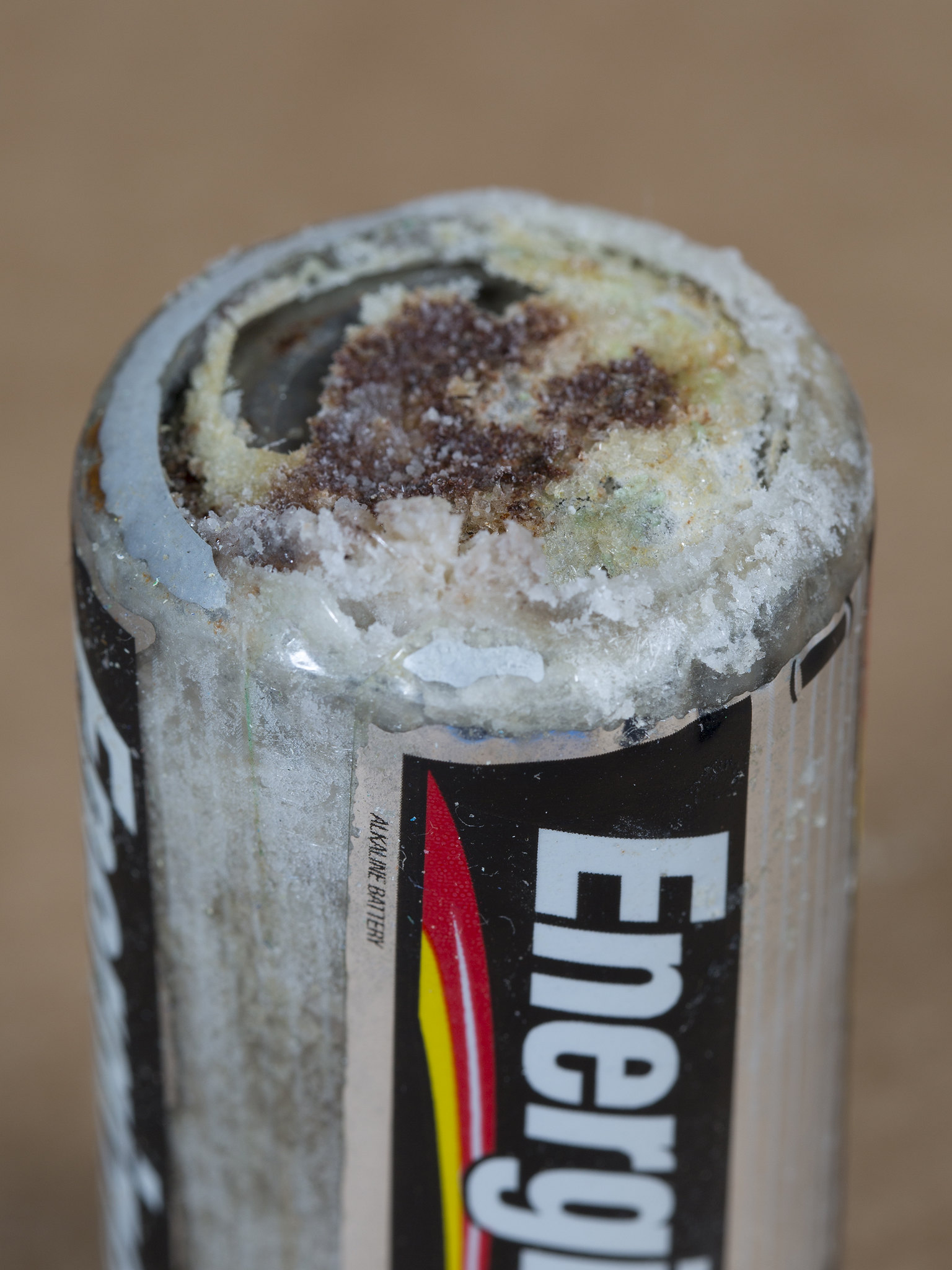 Image shows the end of a battery which has leaked its acidic contents. The leak looks like a thick crust of a whitish substance.
