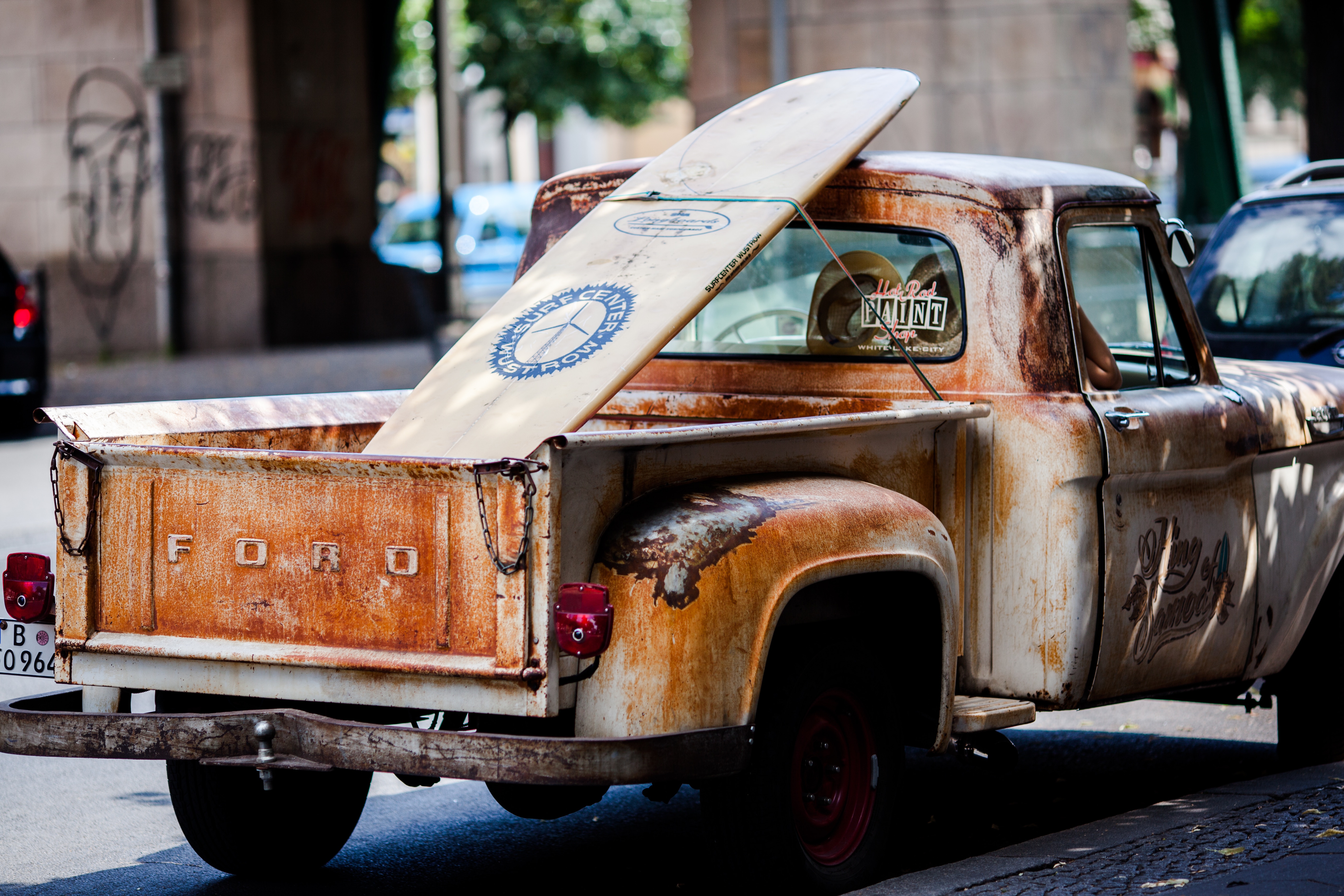 Image shows a very rusty Ford truck with a surfboard in the back.