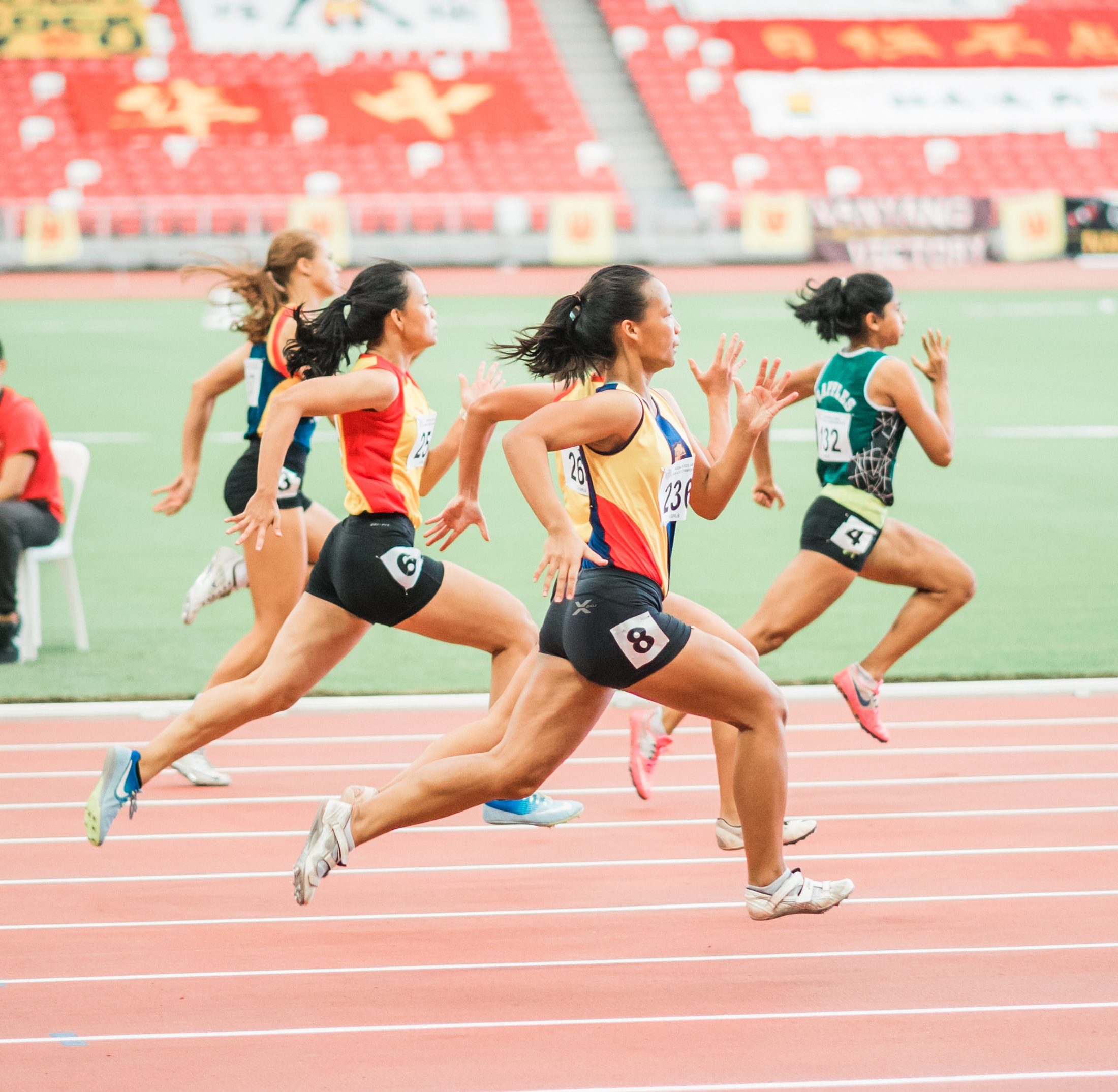Image shows a photo of women in a short distance running race on a track.