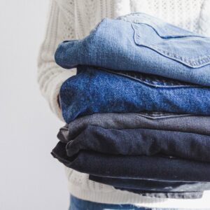Image shows a person holding a pile of jeans of various shades of blue.