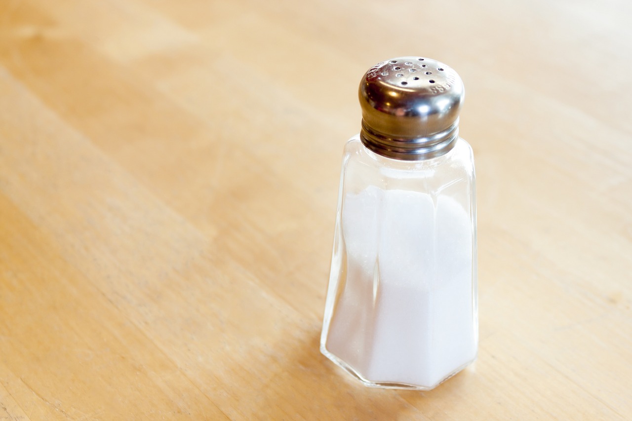 Image shows a salt shaker filled with salt sitting on a wooden counter.